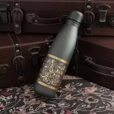 Garrafa térmica verde-escuro com padrão floral colorido e detalhes dourados entre malas de couro castanho escuro