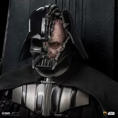 Figura de Darth Vader com capacete danificado e rosto queimado, roupa preta e escudo metálico.