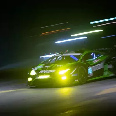 Carro de corrida desportivo preto e amarelo em pista à noite com luzes acesas