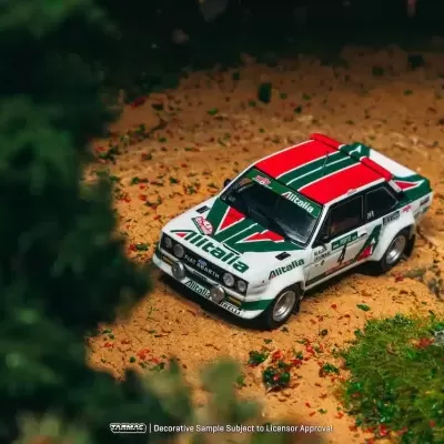 Miniatura de carro de rali branca com detalhes em verde e vermelho em cenário de terra e vegetação.