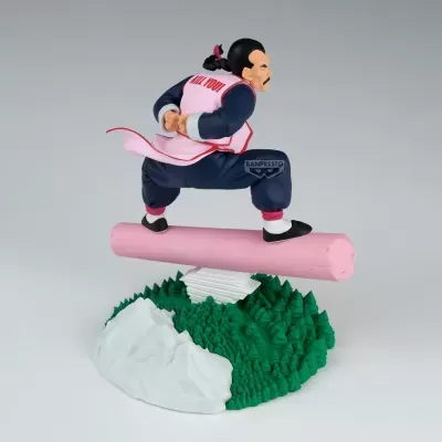 Estátua de personagem masculino em colete rosa e calças azuis sobre tronco rosa em base com árvores verdes e montanha branca