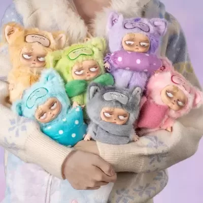 Seis bonecos pequenos de pelúcia coloridos com orelhas e expressões cansadas, segurados por pessoa com camisola de inverno