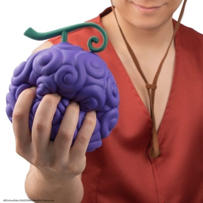 Brinquedo em forma de fruta roxa com padrão ondulado e haste verde na mão de pessoa com camisa vermelha