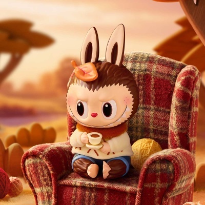 Boneco de vinil com cabeça de coelho numa poltrona xadrez a segurar chávena pequena.