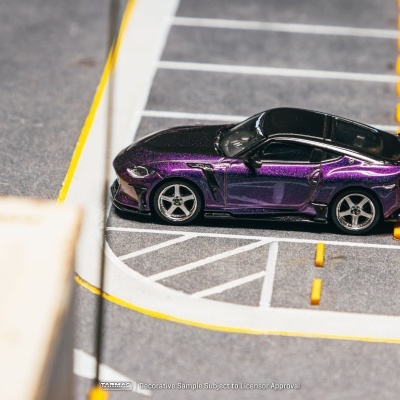 Miniatura de carro desportivo roxo metálico com capô e tejadilho pretos num parque de estacionamento em miniatura