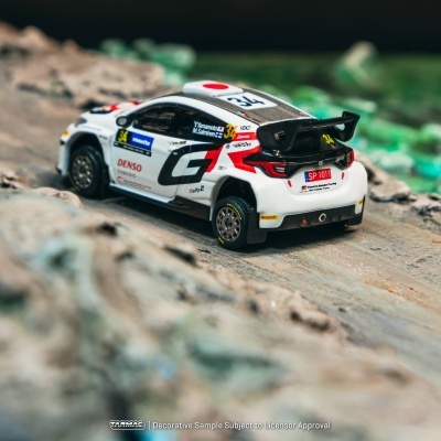 Miniatura de carro de corrida branco com detalhes em preto e vermelho colocado sobre estrada de terra.