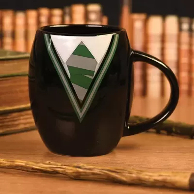 Caneca preta com design de gravata verde e cinza sobre mesa de madeira com livros