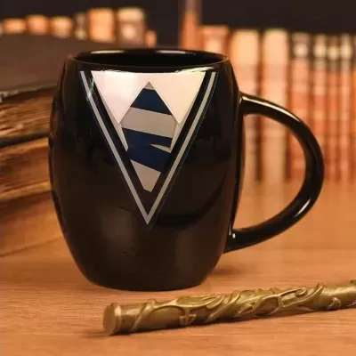 Caneca preta com símbolo triangular branco e azul e varinha dourada sobre mesa de madeira