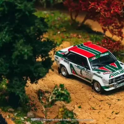 Miniatura de carro de rali Fiat Abarth com decoração Alitalia em estrada de terra com vegetação.