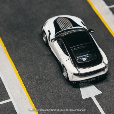 Miniatura de carro desportivo branco e preto numa superfície tipo parque de estacionamento.