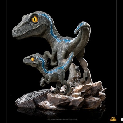 Estátua de velociraptors cinzentos com olhos amarelos e detalhes azuis sobre base de rochas