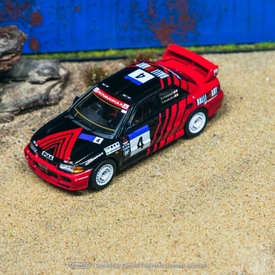 Miniatura de carro de rali preto e vermelho num cenário de areia com pedras e fundo azul.