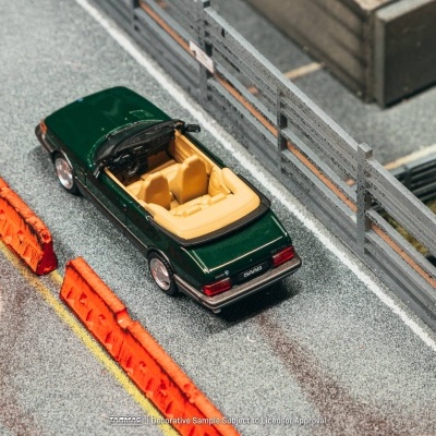 Miniatura de carro conversível SAAB verde com interior bege numa pista com barreira laranja e cerca cinza.