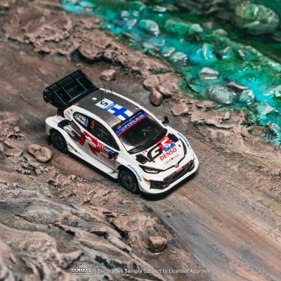 Miniatura de carro de rali branco numa superfície rochosa com água verde-turquesa ao lado