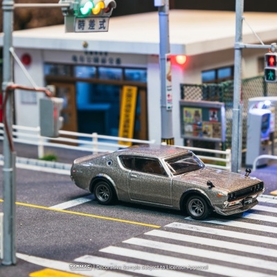 Modelo de carro cinza metálico numa miniatura de cruzamento com sinais de trânsito coloridos e placas