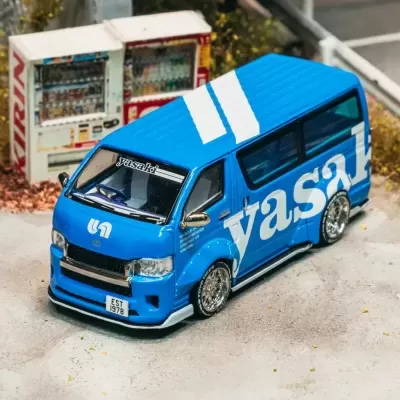 Miniatura carrinha azul com texto branco e jantes cromadas em cenário urbano com máquinas vending