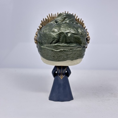 Boneco estilizado com vestido azul e cabeça grande verde com picos dourados