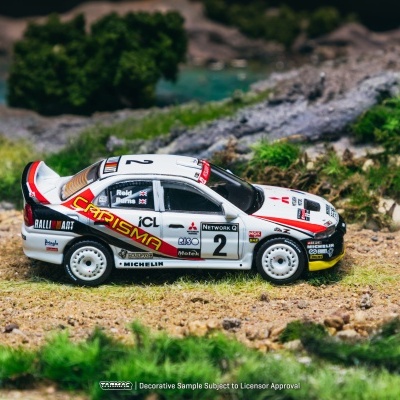 Carro de rali miniatura branco com detalhes vermelhos, pretos e amarelos numa paisagem de relva e terra