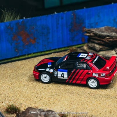 Miniatura de carro de rali Mitsubishi preto e vermelho com vários logos e números 4 junto a cercas e pedras.