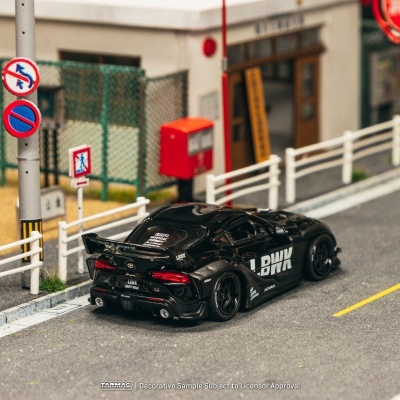 Carro desportivo preto em miniatura numa estrada de miniatura com cercas brancas e sinais de trânsito.
