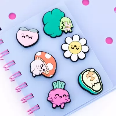 Pins de borracha coloridos em forma de frutas e vegetais sobre caderno azul.
