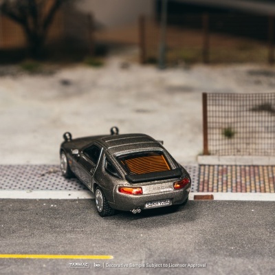 Miniatura de carro desportivo cinzento metálico estacionado numa superfície asfaltada com cerca metálica