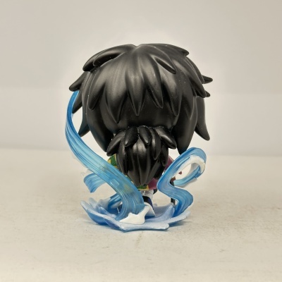 Figura de vinil de personagem com cabelo preto e faixa azul translúcida num fundo cinza.