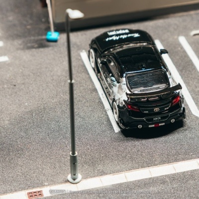 Miniatura de carro preto com detalhes metálicos estacionada num parque de estacionamento em modelo reduzido