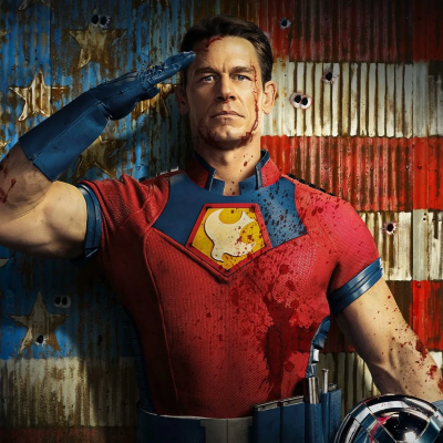 Homem em fato de super-herói vermelho e azul com luva, sangue e continência diante de parede com bandeira US envelhecida