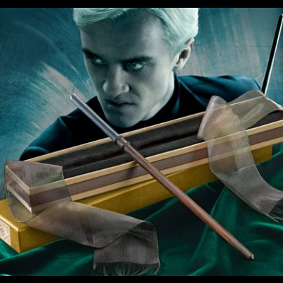 Varinha mágica em caixa amarela e preta sobre tecido verde com personagem atrás