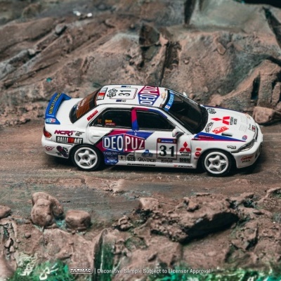 Miniatura de carro de rali branco com detalhes azuis e vermelhos num cenário rochoso.