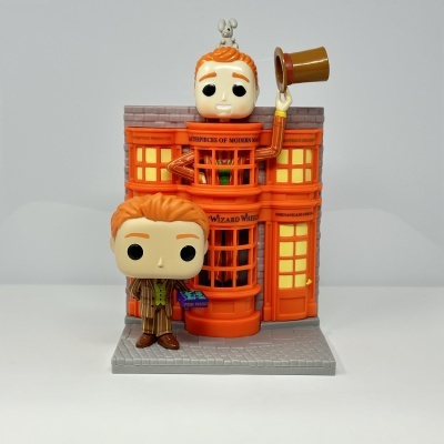 Funko Pop com duas figuras à frente de edifício laranja com texto