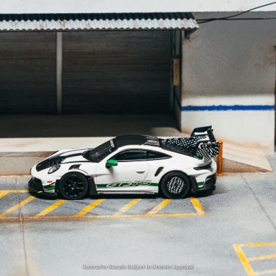 Miniatura carro desportivo branco GT3 RS com detalhes verdes e pretos junto a edifício cinzento com portas metálicas