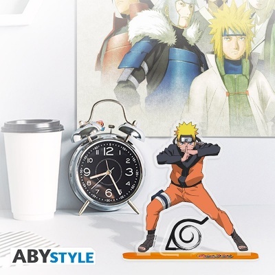 Figura acrílica do personagem Naruto Uzumaki em pose de artes marciais, relógio despertador e copo descartável em mesa branca