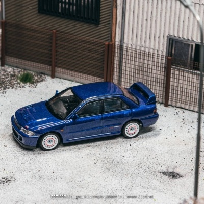 Miniatura de carro desportivo azul metálico com jantes brancas e detalhes vermelhos em cenário exterior