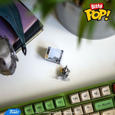 Miniatura Funko Pop! de personagem prateado com caixa pequena ao lado sobre mesa branca com teclado colorido