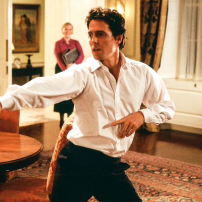 Homem de camisa branca e calças pretas em sala com carpete estampado e móveis clássicos