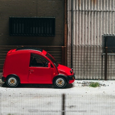 Miniatura de carrinha vermelha estacionada ao lado de parede e vedação metálica