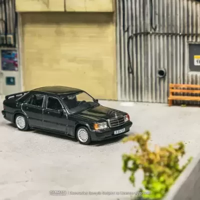 Modelo em miniatura de um carro preto Mercedes-Benz numa oficina com pneus e banco de madeira