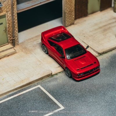 Carro desportivo vermelho estacionado numa rua em frente a porta verde de edifício de tijolos