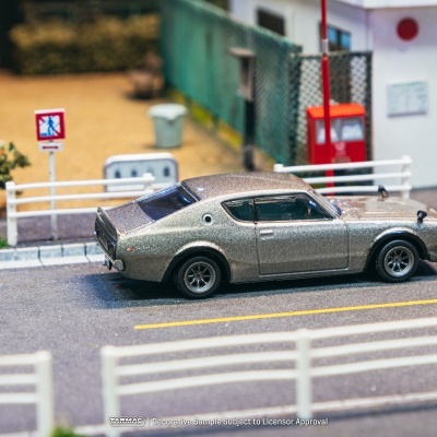 Miniatura de carro clássico cinza numa rua com sinais de trânsito e barreiras brancas