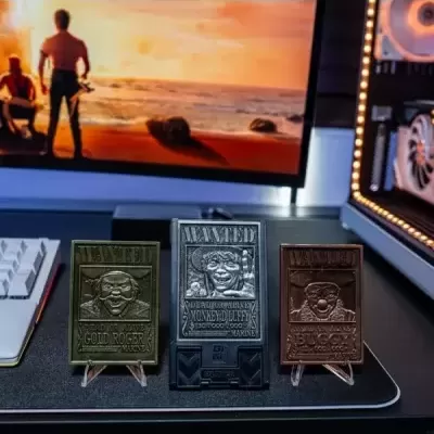 Três placas metálicas 'WANTED' com retratos de personagens, sobre mesa com teclado e monitor ao fundo