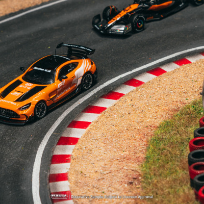 Miniatura de carro de corrida laranja e preto numa pista curva com marcas brancas e vermelhas