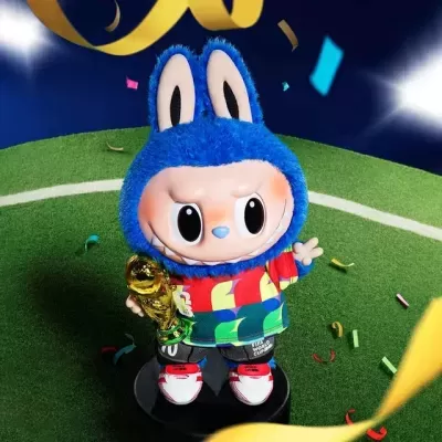 Figura colecionável com capuz azul, roupa colorida, segurando troféu dourado num campo de futebol em miniatura
