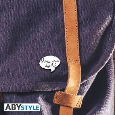 Mochila azul escuro com tira castanha e pin com frase 'How you doin?'