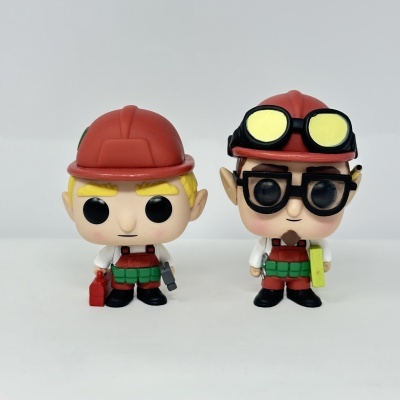 Duas figuras Funko Pop de construção com capacetes vermelhos e roupas brancas e verdes.