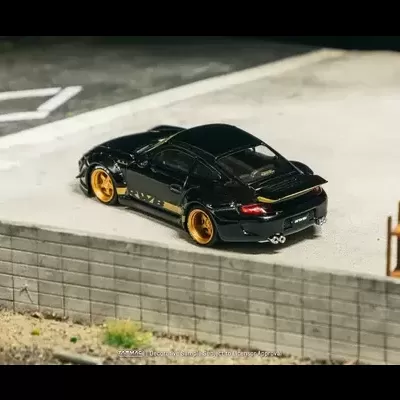 Miniatura de carro desportivo preto com rodas douradas junto a muro de blocos