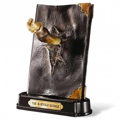 Livro falso castanho escuro com varinha saindo do meio e placa com texto 'TOM MARVOLO RIDDLE'.