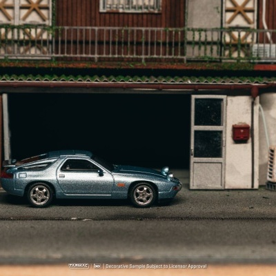 Miniatura de carro desportivo azul metálico estacionado junto a uma garagem em miniatura