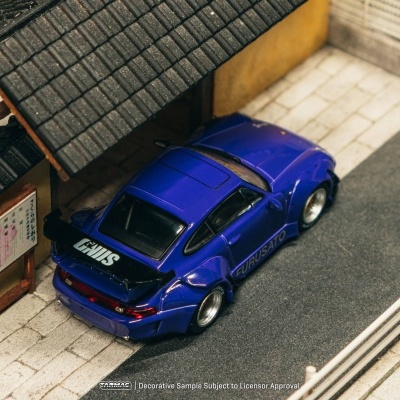 Modelo de carro desportivo azul com spoiler preto estacionado numa miniatura de rua com casa amarela e pavimento cinzento